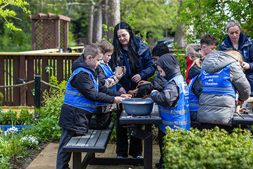 A group of children wearing RSPCA tabards in a garden, two adults are assisting