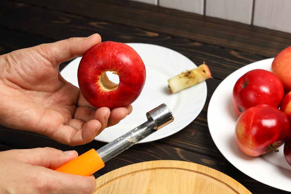Person holding a red apple with the core removed using an apple corer.