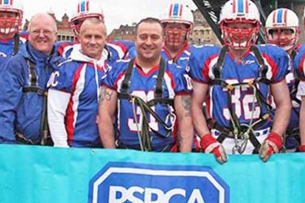 Men in blue shorts and headgear standing in a group in front of an RSPCA banner