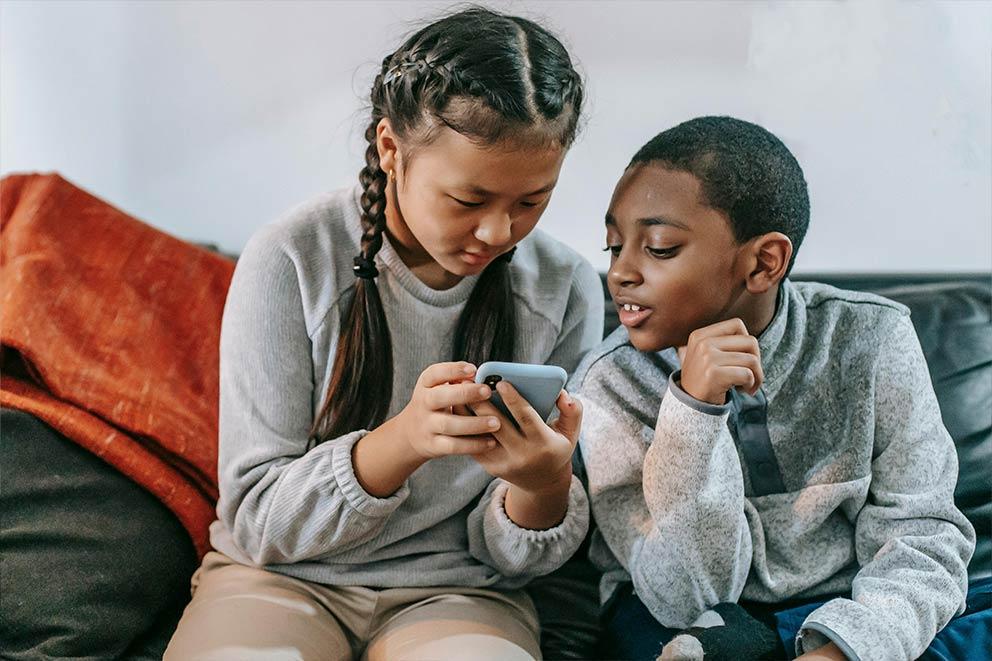 Two children sitting on a sofa looking at a mobile phone.