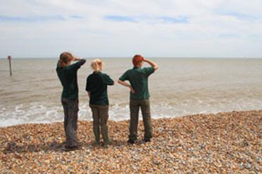 Three people are stood on a pebble beach looking out to shore