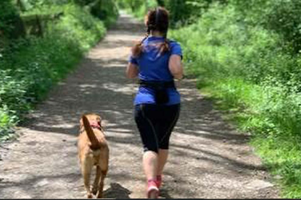 A female runner out running with a dog in the countryside.