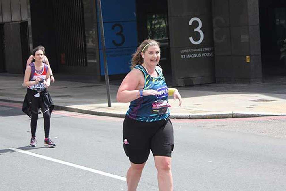 Smiling female fundraiser running with a Team Animal vest on an organised charity running event.