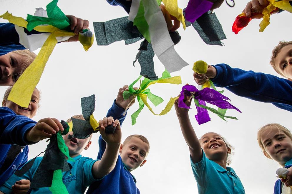 A group of children hold coloured paper strips in a circle