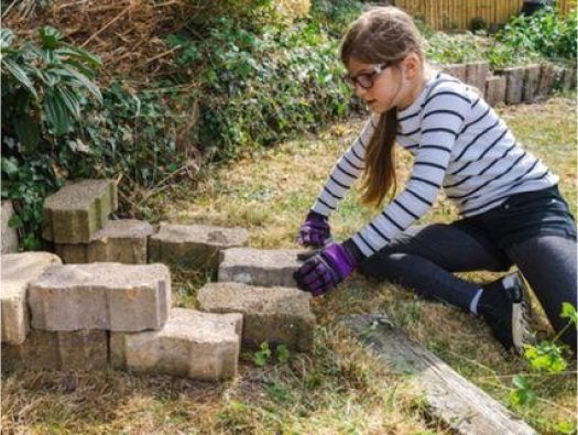 Young girl building a hedgehog house out of bricks in the garden.